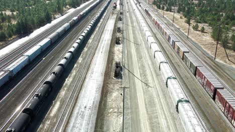 backwards flight dolly wide drone shot flying over a railroad station in a desert environment on a sunny day next to a highway and a river and mountains in the background and powerines in the picture