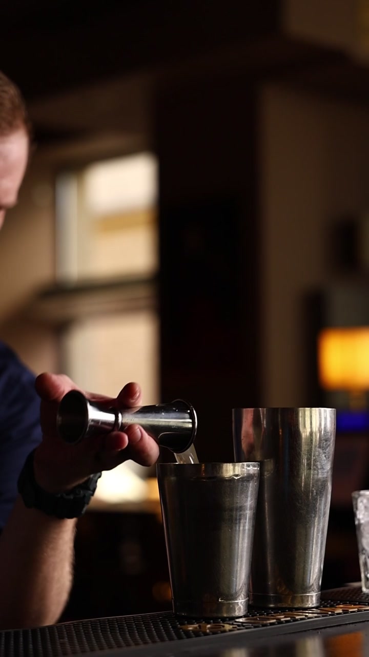 Bartender hælder væske fra en jigger i en cocktailshaker