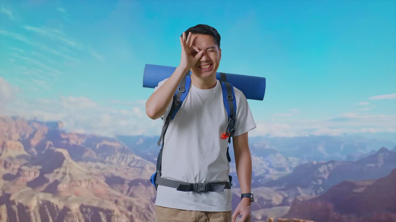 Asian Male Hiker With Mountaineering Backpack Smiling And Showing Ok Sign With Fingers Over Eyes While Traveling At The Top Of Mountain