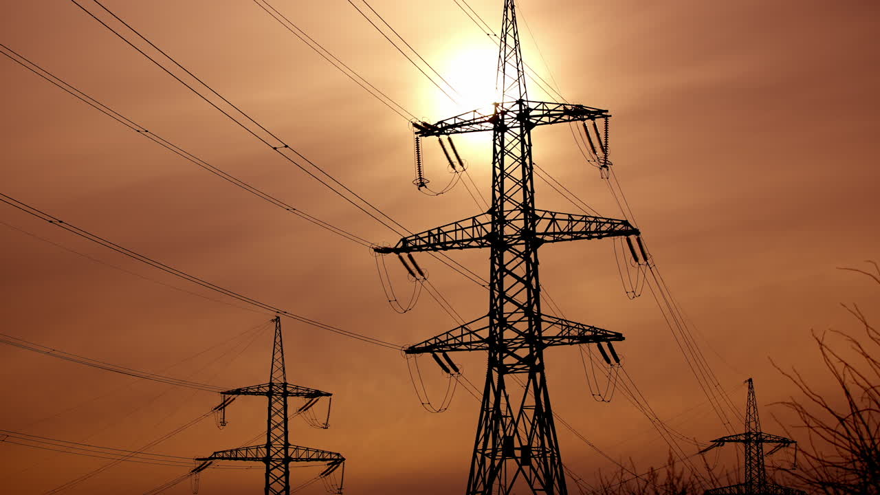 Transmission lines against the evening sky. High-voltage electric towers with wires on the setting sun background. Black pylons with electricity.
