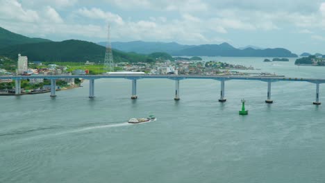 a bridge joins geojedo island to the south korean mainland with a barge pulling cargo - static, wide angle view