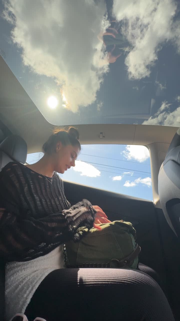 Woman in car backseat, looking at phone.