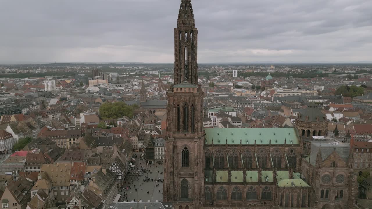 Spettacolare vista aerea dell'intricata guglia gotica della Cattedrale di Strasburgo che si erge sopra il centro città, con architettura dettagliata, i tetti circostanti e la vivace piazza della città visibile sotto.