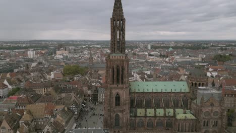dramatic aerial view of strasbourg cathedral’s intricate gothic spire rising above the city center, with detailed architecture, surrounding rooftops, and the vibrant town square visible below
