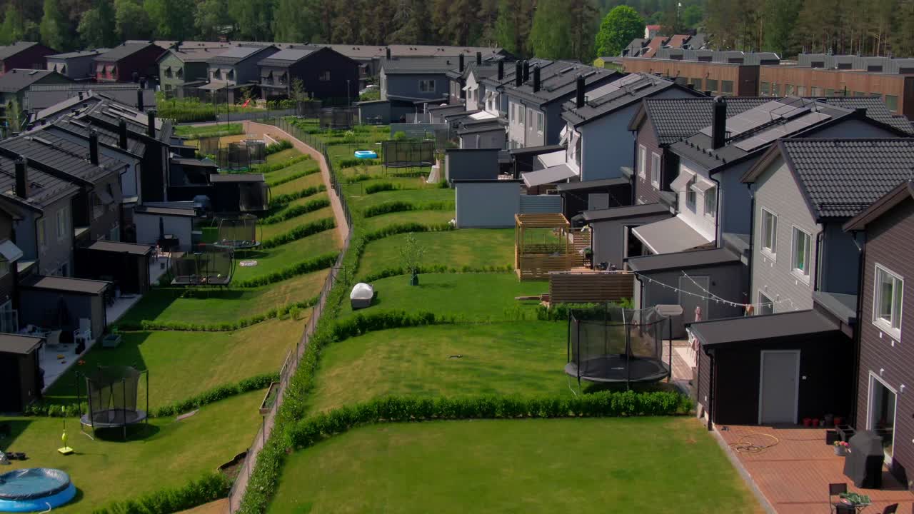 Fly through view of the rear of contemporary row houses, showing fenced yards, solar panels, and steeply sloped green areas