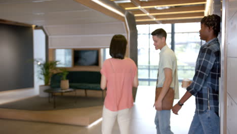 walking through modern office, three colleagues discussing work and using tablet