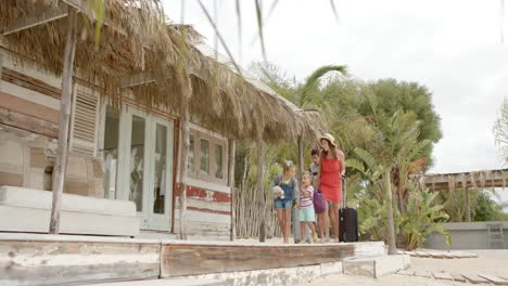 Happy-caucasian-family-walking-with-luggage-at-beach-house