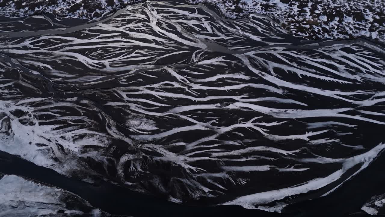 Dramatic aerial drone shot of a river winding through volcanic terrain in Iceland, with intertwining flows creating a poetic natural pattern