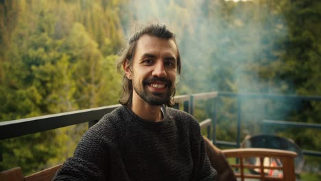 un joven moreno con un suéter verde posa en un picnic con vistas a las montañas y el bosque de coníferas. retrato de un hombre feliz descansando fuera de la ciudad
