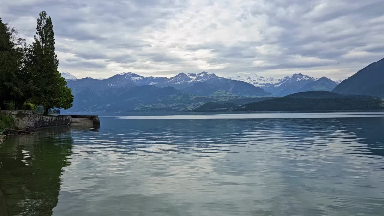 스위스  호수 (swiss thun lake) 의 정적, 배경에는 눈 어리 산과 구름을 통해 빛나는 빛이 있습니다.