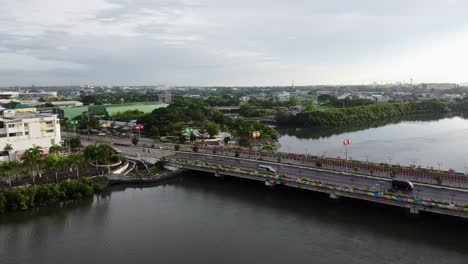 panning left to right drone footage from a river to overlooking an urban city filled with trees in the philippines called iloilo on a cloudy morning