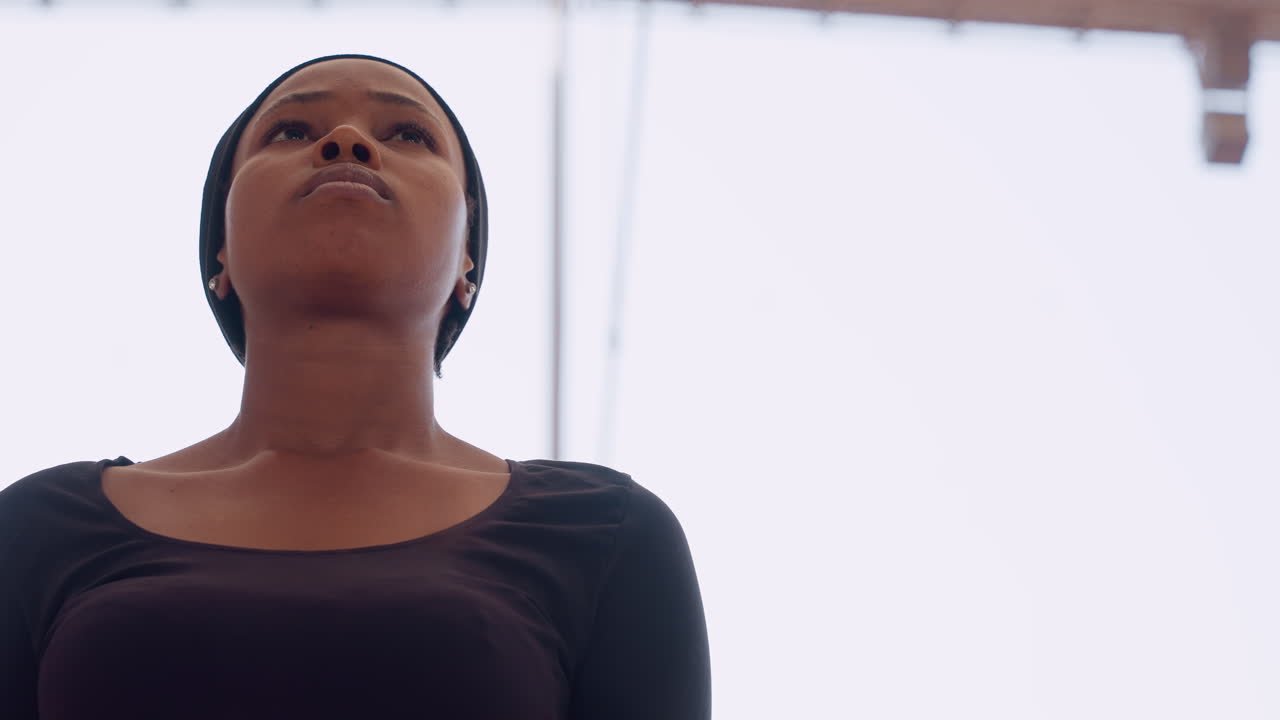 black woman looking upward and focused, lowangle training portrait under stadium canopy, headband visible, beads of sweat, tense jaw, breath control, cinematic sports vibe, empowerment energy