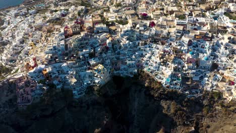 giro aéreo de arriba hacia abajo sobre el famoso pueblo griego oia con casas cueva blancas y villas en santorini, grecia