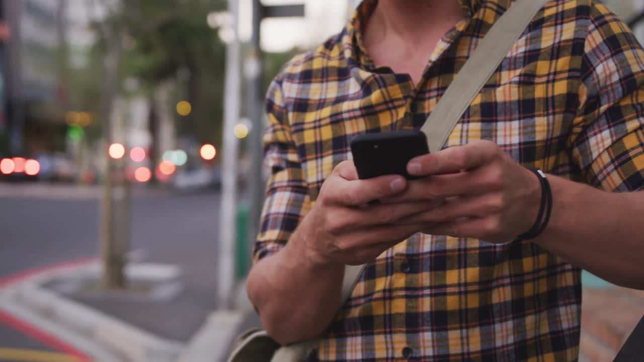 hombre caucásico sonriendo y usando su teléfono en una calle