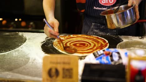 chef spreads sauce on pizza dough