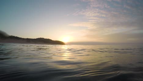 The-sun-rising-over-the-ocean-from-within-the-water-with-the-waves-passing-by