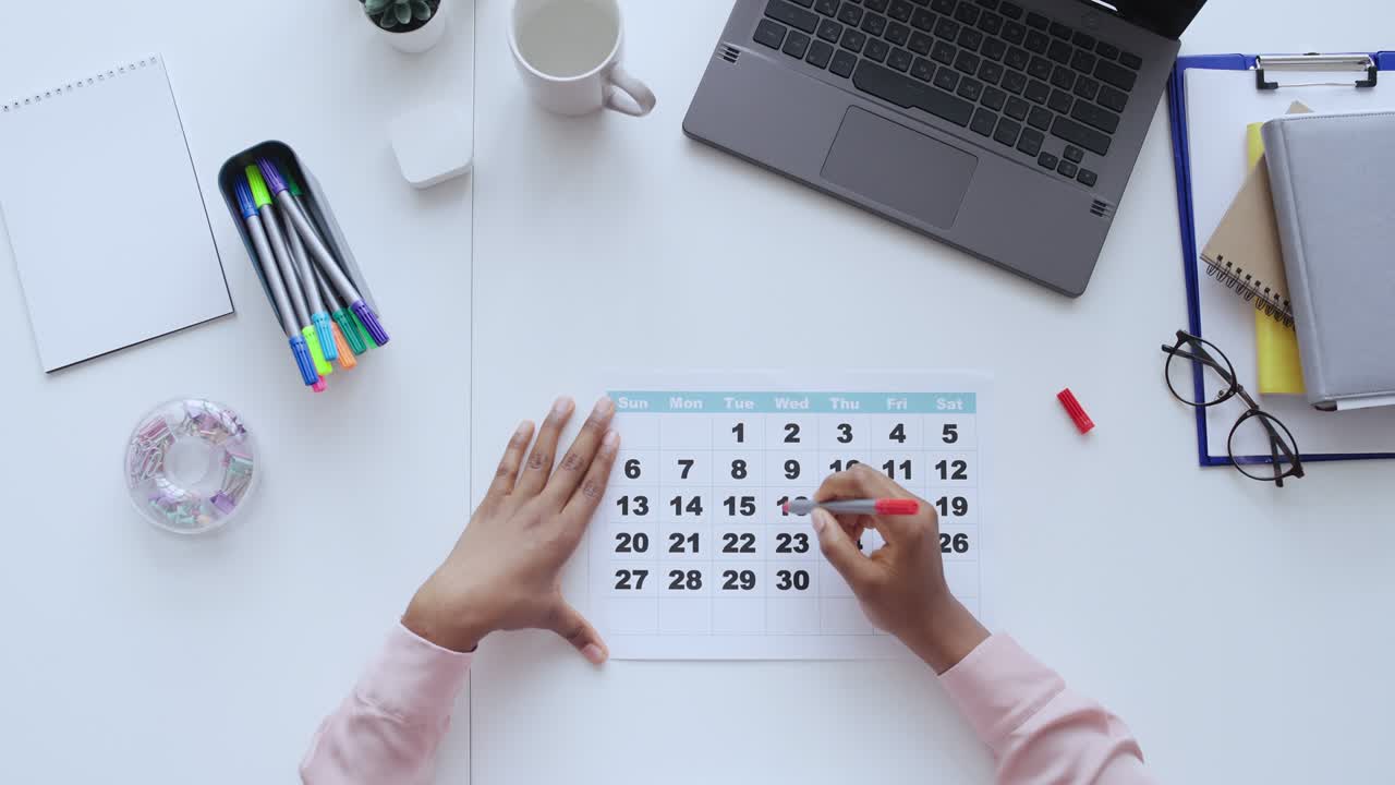 Top view of woman circling date on paper calendar, planning a meeting, deadline