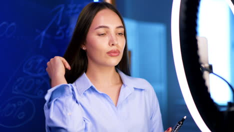 beautiful dark-haired caucasian woman in shirt records video pointing at glass wall with written numbers. blog footage indoors.