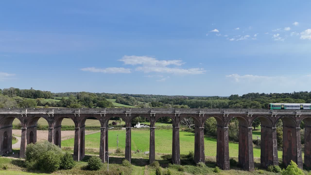 Aerial view of the iconic Ouse Valley Viaduct in Sussex, England, as a passenger train glides across its arches. Historic Victorian bridge surrounded by scenic countryside