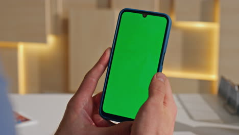 man hand holding greenscreen smartphone in office closeup. unrecognizable worker
