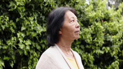 senior asian woman enjoying peaceful moment outdoors, surrounded by lush greenery
