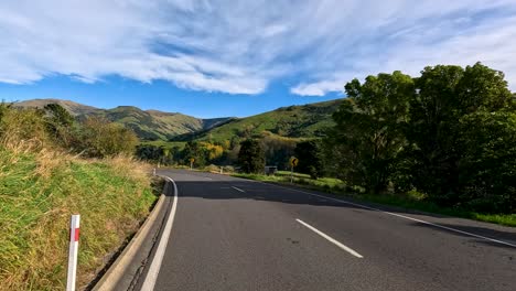 a vehicle travels a curving country road through green hills and farmland under bright daylight, with smooth camera movement and scenic landscape views