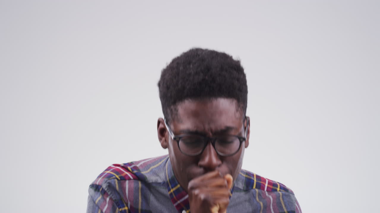 a handsome young man coughing against a grey