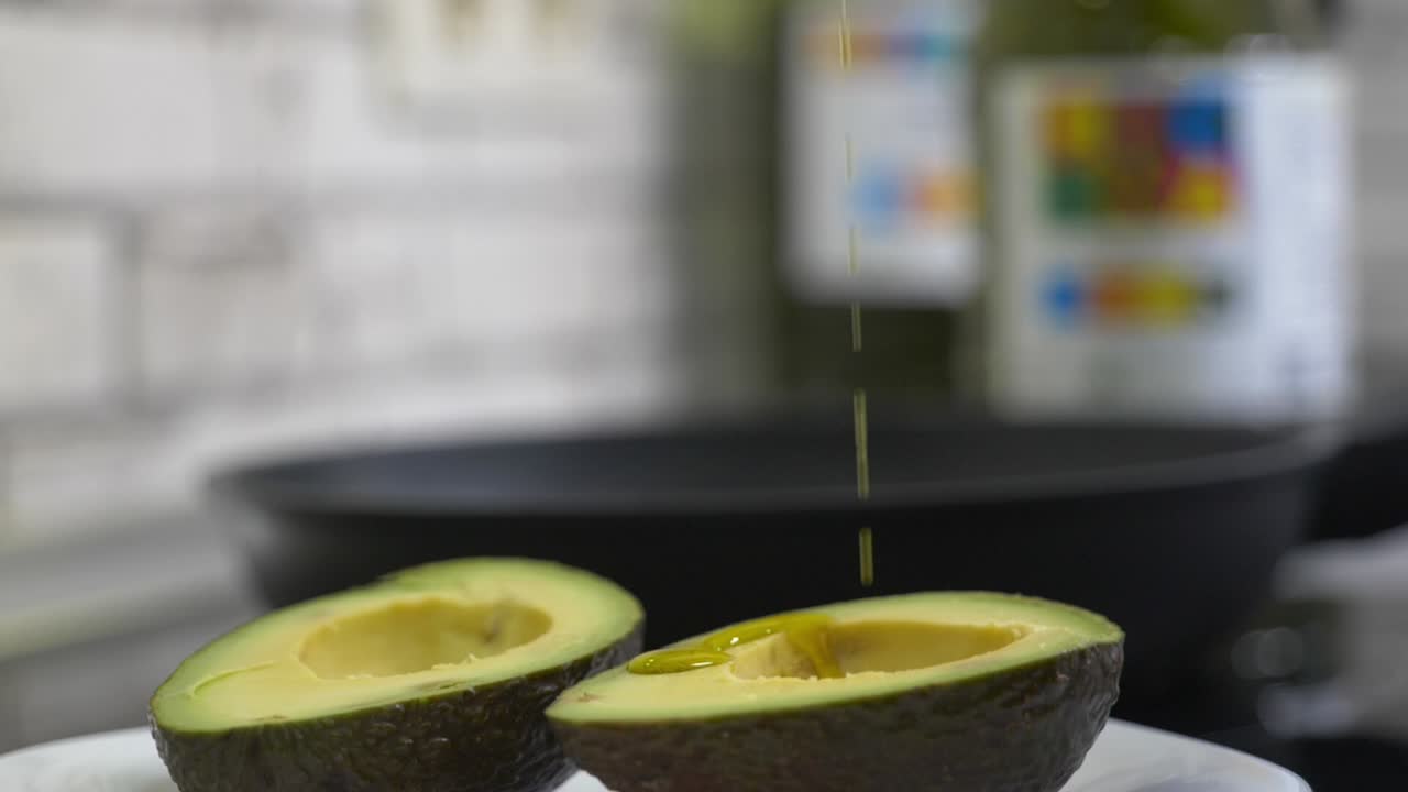 Olio extra vergine d'oliva (EVOO) versato su avocado appena tagliato. Una combinazione di grassi sani, essenziali nella dieta mediterranea e nella cucina sana.