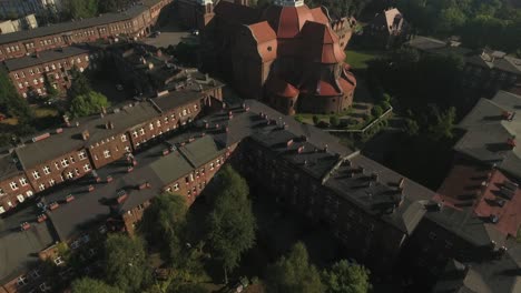 a green square with trees in the historic mining settlement of nikiszowiec, featuring an old church, on a sunny summer day, in 4k