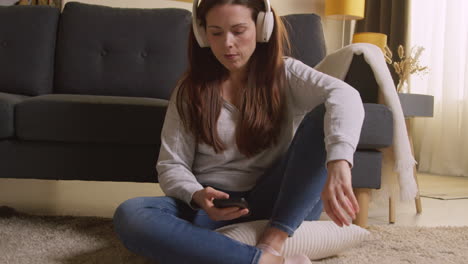 woman wearing wireless headphones sitting on floor at home streaming music from mobile phone 4