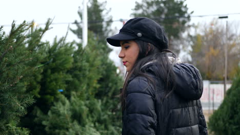 A-hispanic-woman-shopping-for-a-seasonal-holiday-Christmas-tree-decoration-on-a-lot-with-many-species-of-festive-trees