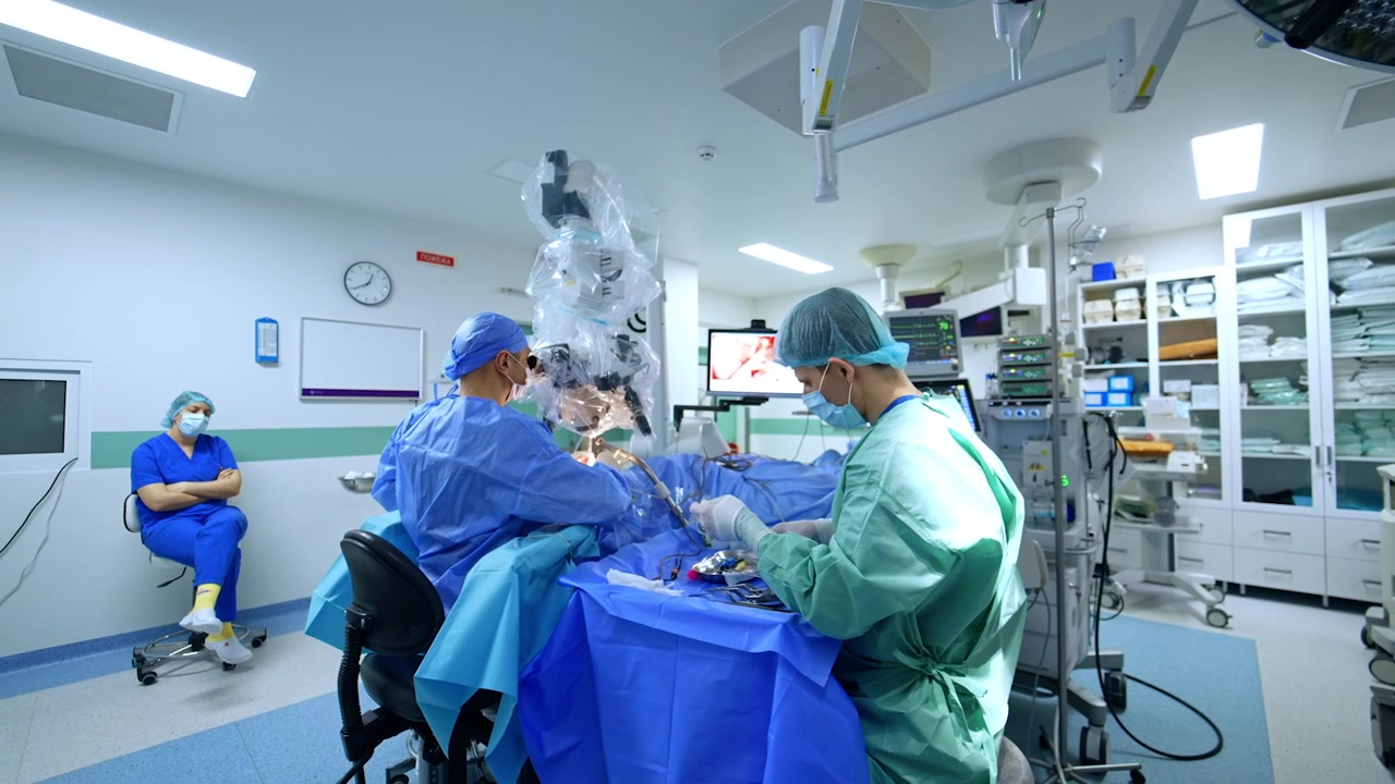 Kyiv, Ukraine, 5 May 2026: Surgical microscope in use during neurosurgery in a modern operating room. Surgeons at operative field, scrub nurse seated, instrument tray and supply cabinets visible.
