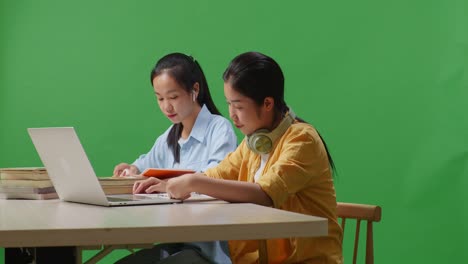 asian woman students reading books while sitting on a table with laptop in the green screen background classroom