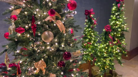 Slow-motion-footage-of-one-large-Christmas-tree-with-ornaments-and-lights,-and-three-smaller-Christmas-trees-grouped-together