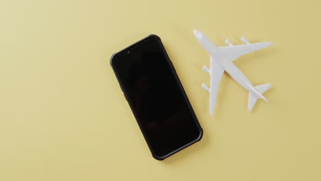 Close-up-of-white-plane-model,-smartphone-and-copy-space-on-yellow-background