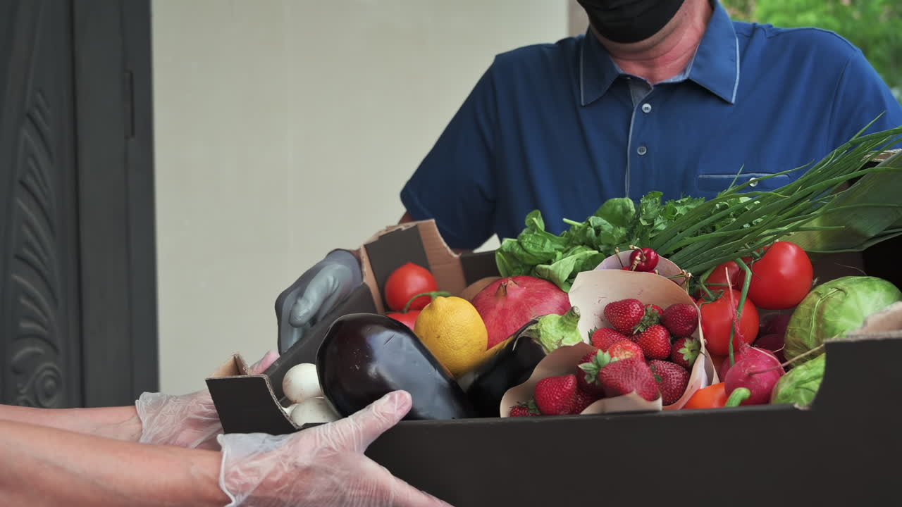 Close up of a man wearing gloves holding a box full of fresh fruits and vegetables