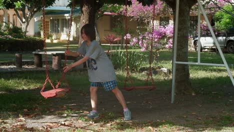 young, black-haired, lonely girl plays on swing set alone and pushes empty swing -static medium shot