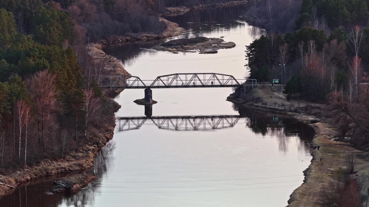 Vista aerea di un ponte a traliccio metallico che attraversa un fiume tranquillo al tramonto
