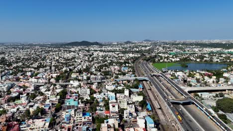 aerial drone footage of a cityscape in chennai, india, on a clear, sunny day. over a multi-lane flyover bustling with vehicle traffic, including cars, trucks, and buses. parallel to the flyover train