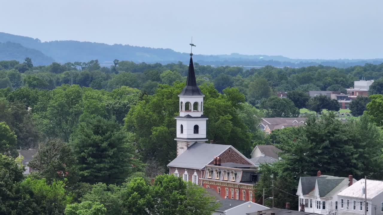 Aerial orbit shot of church tower in american town during sunny day in summer. Green trees in american neighborhood of historic town. Wide shot