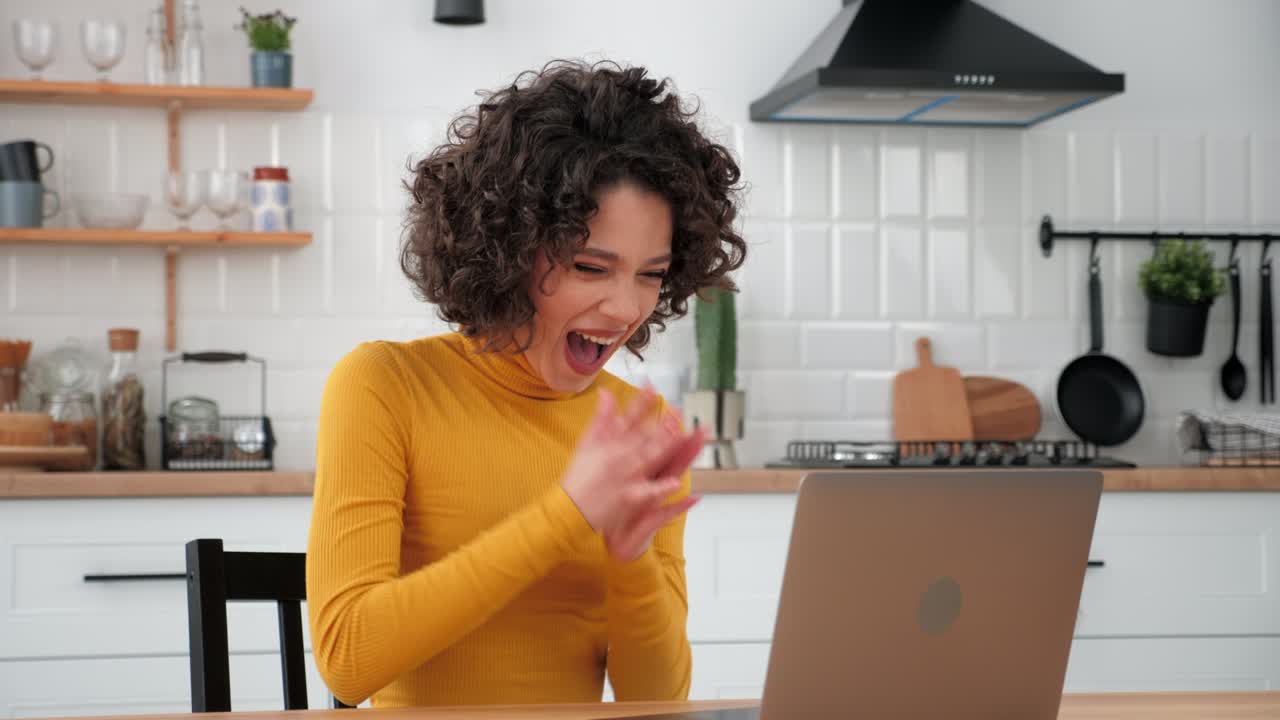 Excited curly woman student uses laptop celebrating admission to university