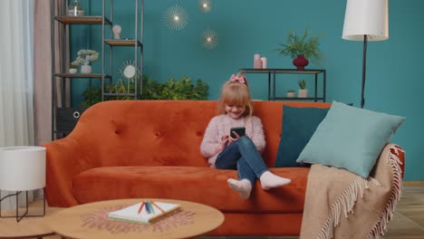 niña de escuela primaria usando un dispositivo de tecnología de teléfono móvil sentada en el sofá sola en casa