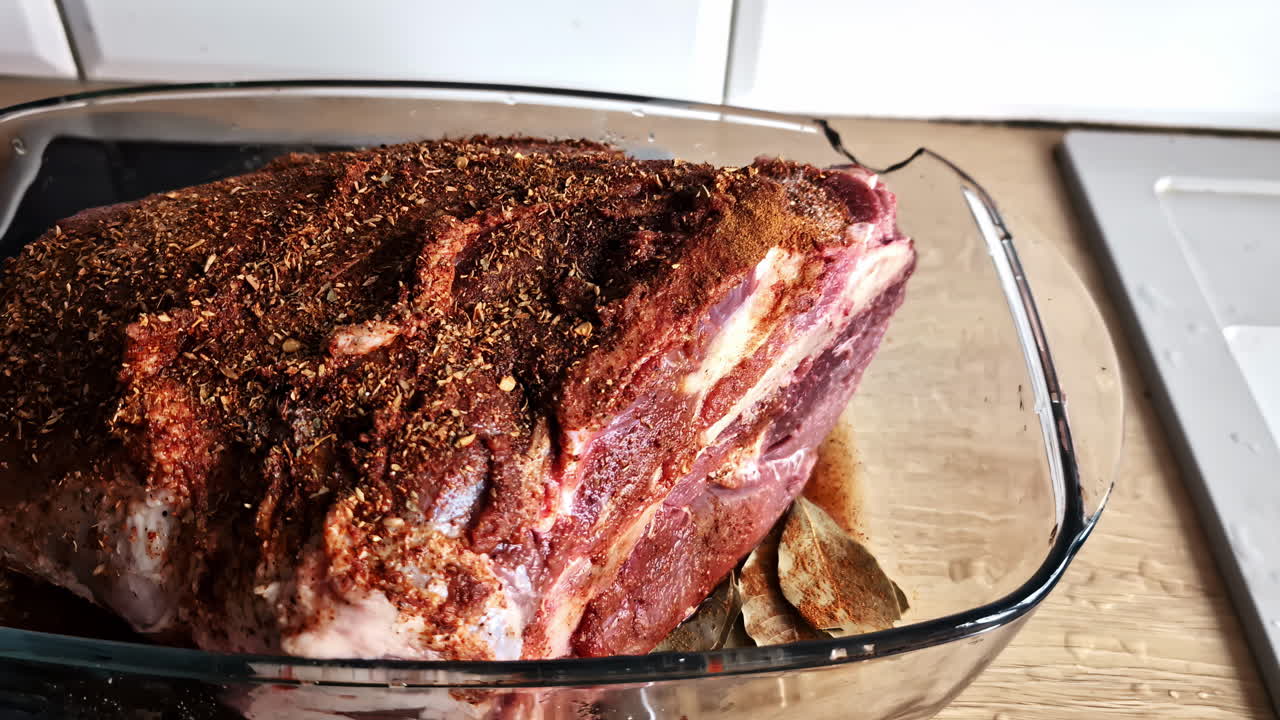 Raw meat seasoned with spices in a glass pot, prepped and ready for cooking, full of flavor.