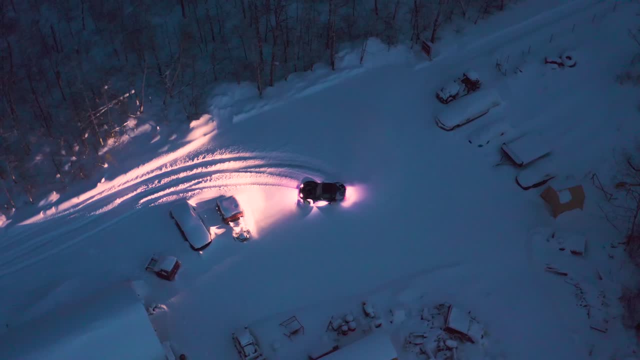 una vista de pájaro de un coche miata todoterreno hecho a medida haciendo donuts en un aparcamiento con nieve fresca