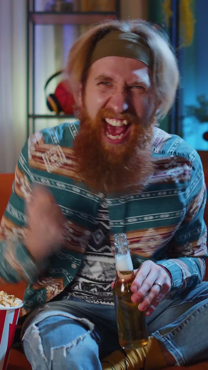 Mand sidder på sofaen, spiser popcorn og ser en spændende tv-serie eller sportskamp online derhjemme.
