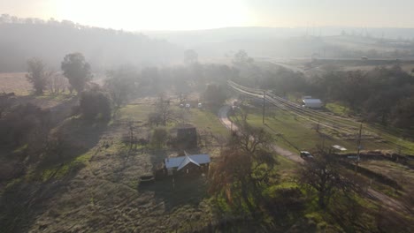 drone footage on a bright misty morning over historic clarksville, california with houses, grassland, trees and farmland below and misty hills in the distance