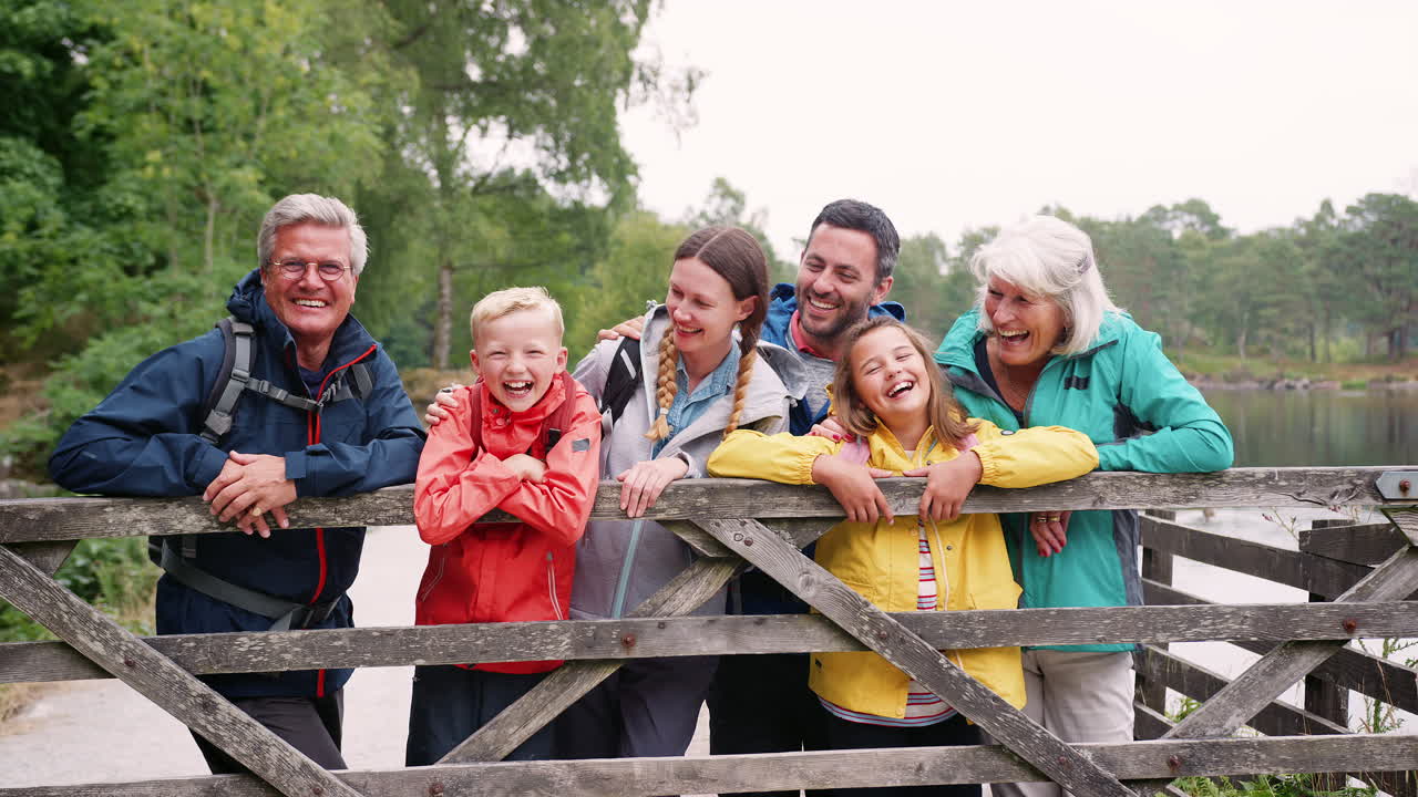 Multi generation family looking at camera standing behind wooden fence, Lake District, UK