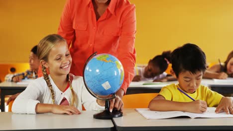 teacher assisting school kids in reading globe in classroom