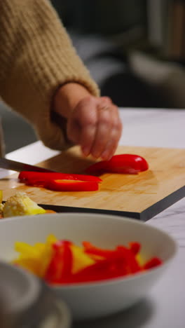 vertical video close up of woman at home in kitchen preparing healthy fresh vegetables for vegetarian or vegan meal slicing red peppers on board 2