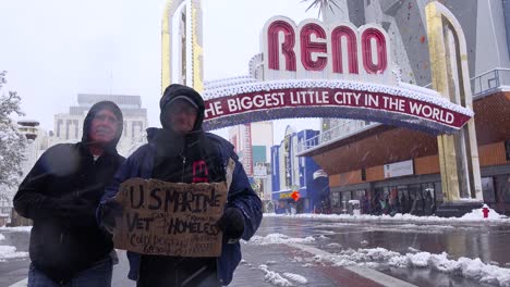 two homeless veterans stand in front of the reno arch begging for money